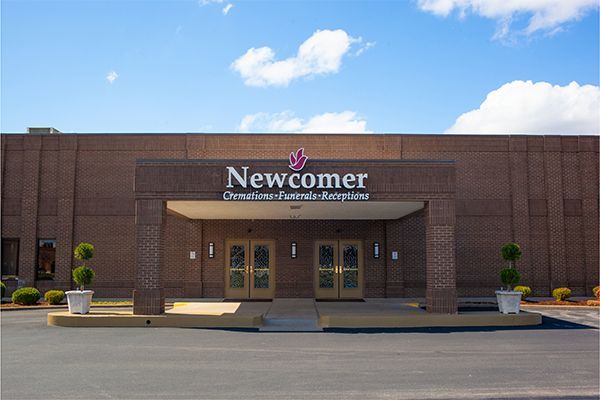 Exterior view of Newcomer Funeral Home, brick building with entrance under a sign; clear sky.