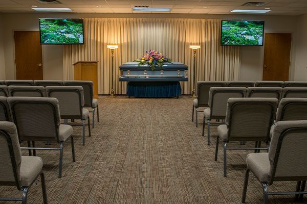 Funeral home with a casket, rows of chairs, and floral arrangements.