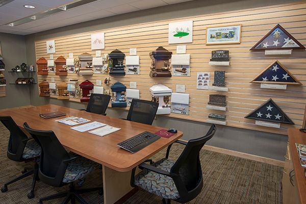 A funeral home office with urns and flag displays on the wall, a conference table, and chairs.