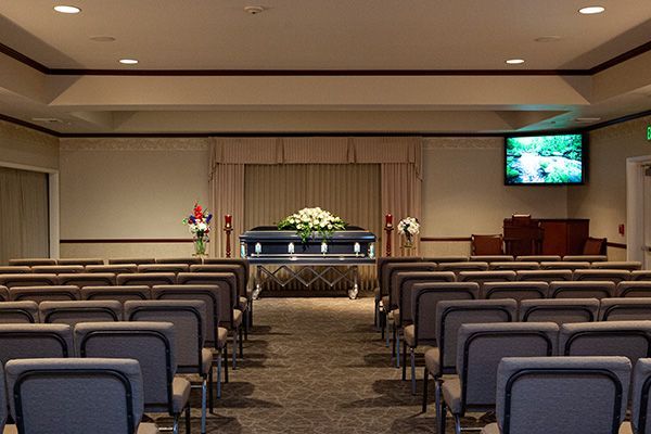 Funeral home interior with a casket, rows of chairs, and a screen.
