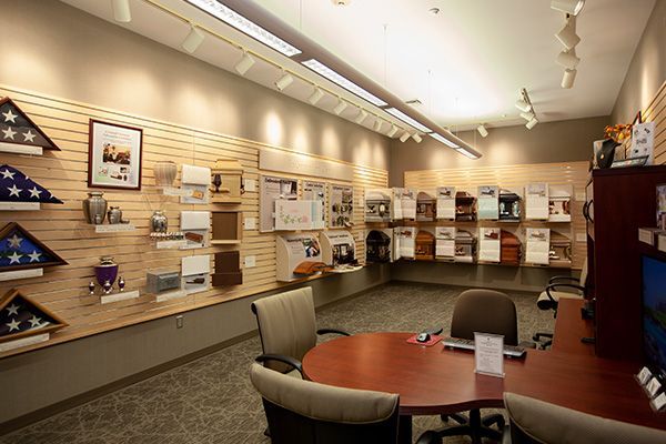 Interior of a funeral home, displaying urns, flags, and planning materials. Brown walls, wood furniture.