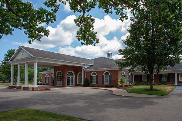 Red brick building with a portico, arched windows, and a driveway. A tree overhangs the building.