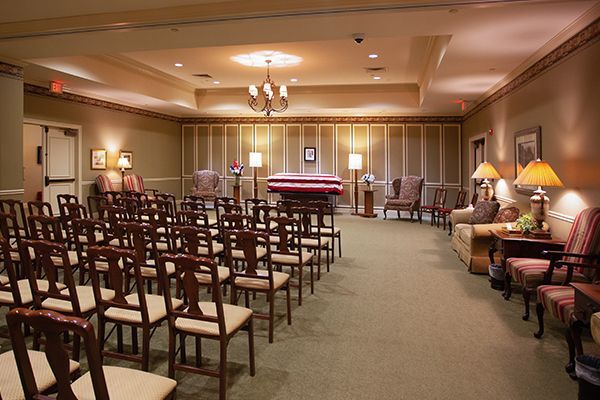 Interior of a funeral home chapel with rows of chairs facing a casket, neutral colors.