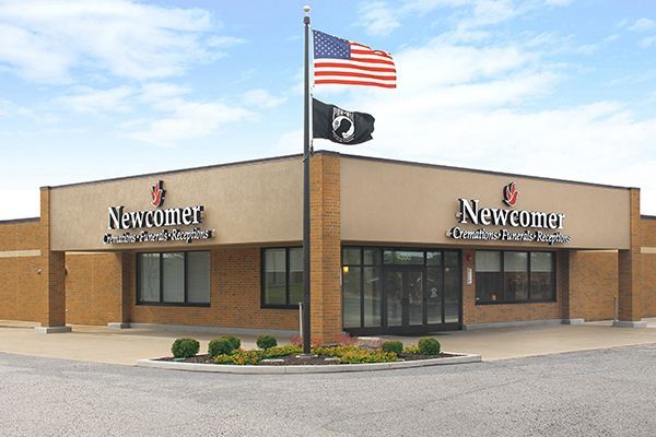 Newcomer Funeral Home building with American and POW/MIA flags. Brick exterior, blue sky.