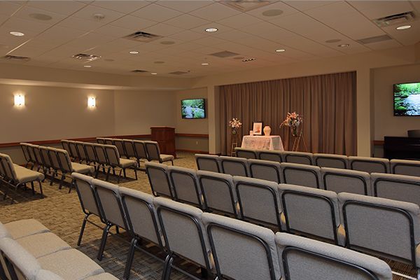 Funeral home chapel with rows of chairs facing a draped altar, flanked by screens.