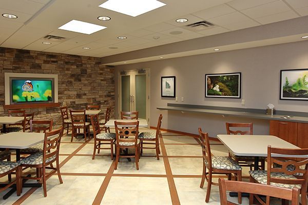 Dining room with tables, chairs, TV on stone wall, and art on gray walls.