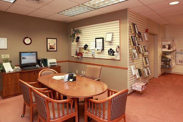 Office with oval table and chairs, computer, and display of brochures. Pink carpet, brown walls.