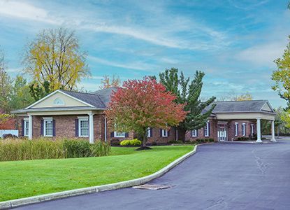 Brick building with a long driveway, green lawn, trees with red and yellow leaves, and a blue sky.