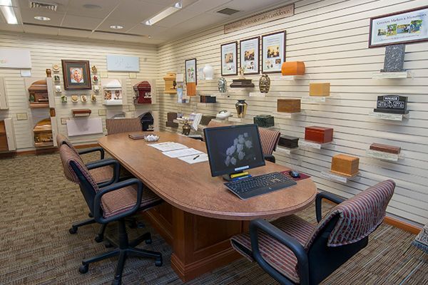A funeral home office with display of urns and a desk with computer and chairs.