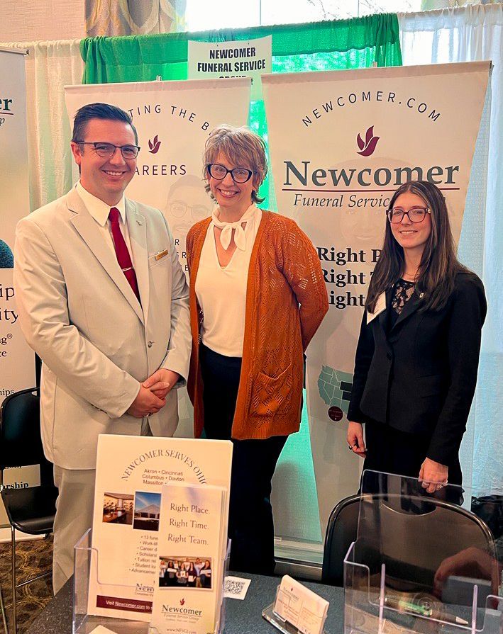 Two men in suits smiling outside a building. The older man has gray hair.