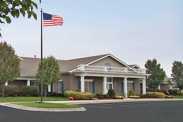Building with American flag, brick facade, white columns, green shrubs, and black asphalt.