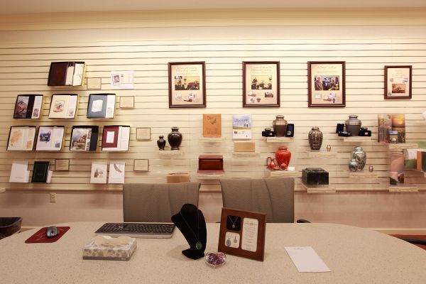 Funeral home display: Urns, keepsakes, and memorial books on shelves and wall, over a table.