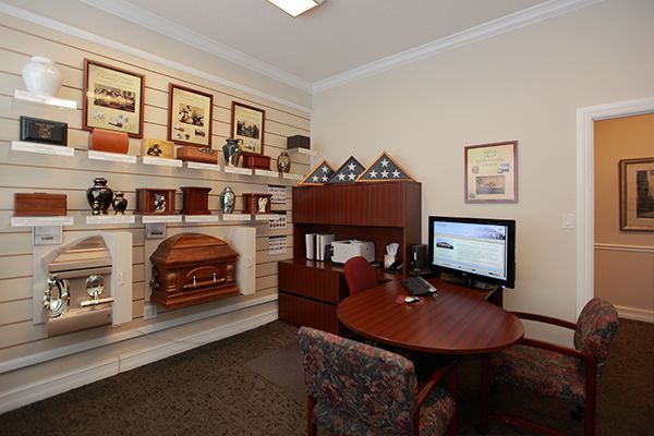 A funeral home consultation room displaying urns and caskets, with a desk and chairs.