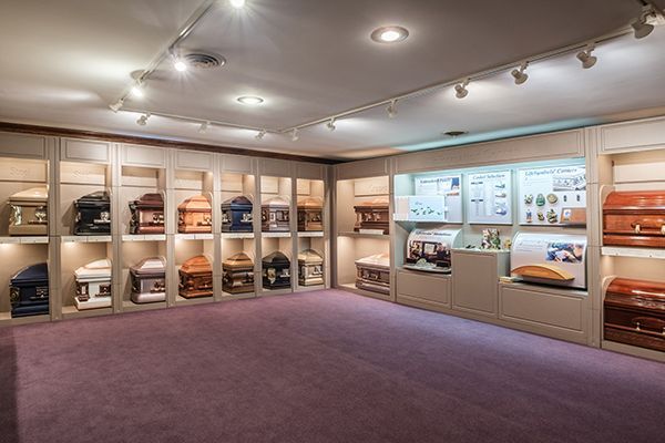 Funeral home display room with caskets on shelves, and informational displays. Purple carpet.