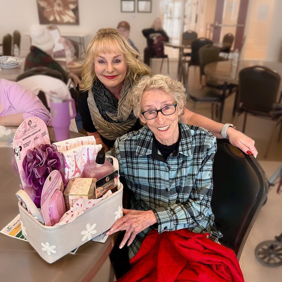 Man in suit hands a check to a smiling woman. They stand with bags of goods in front of a fireplace screen.