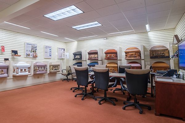A funeral home showroom with caskets on display, several chairs around a table, and brochures on the wall.