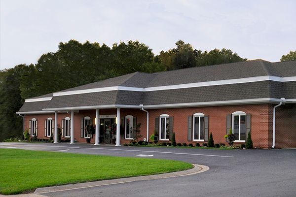 Brick building with white trim and a dark gray roof, on a well-manicured lawn with a curved driveway.