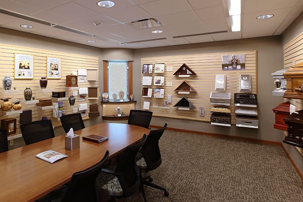 Funeral home display room with urns, caskets, photos, and a meeting table.