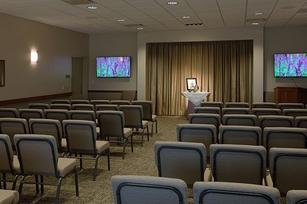 Empty auditorium with rows of chairs facing a small altar with a photo, and two TVs.