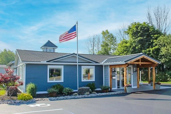 Blue building with US flag, porch, and landscaping under a bright blue sky.