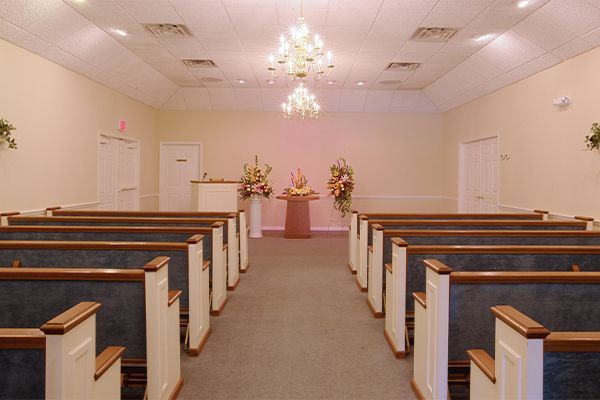 Interior of a funeral home chapel with rows of pews, a podium, and floral arrangements.