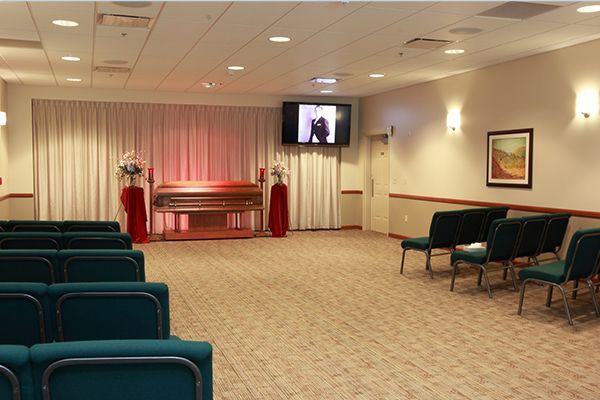Funeral home chapel with a casket, seating, and a screen displaying a video.