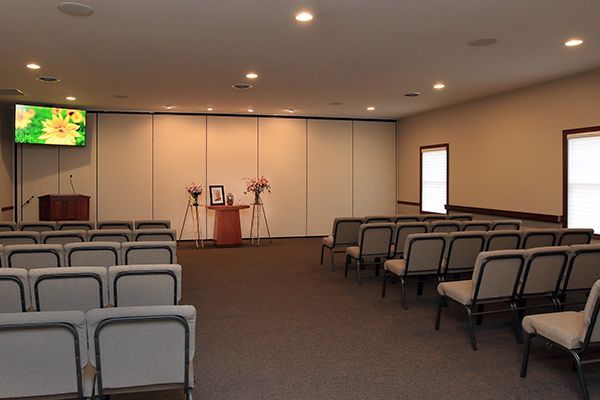 Empty funeral chapel with rows of chairs facing a small altar; beige and brown tones.