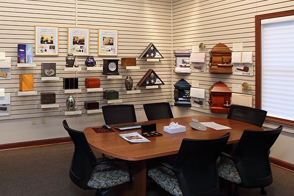 A room with a table and chairs displaying urns. Beige wall with horizontal stripes, and window with blinds.