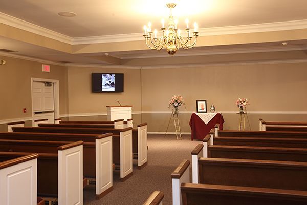 Funeral home chapel with rows of pews, podium, flowers, and a small table with a framed photo.