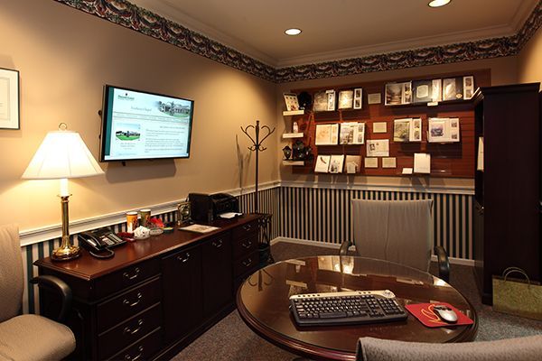 A wood-paneled office featuring a desk, a round table with a keyboard, a display screen, and various decorative items.