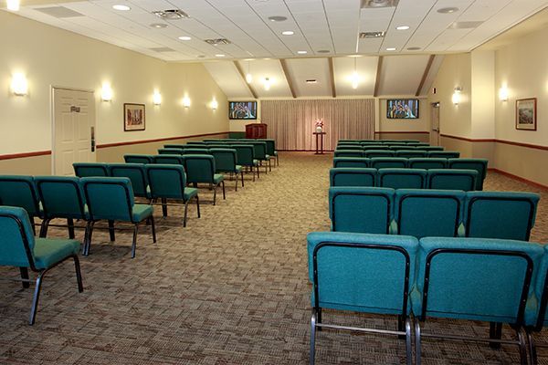 An empty chapel with teal chairs, tan walls, and a raised platform.