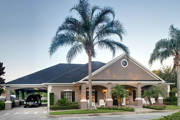 Single-story beige building with black roof, palm trees. A golf cart under a carport.