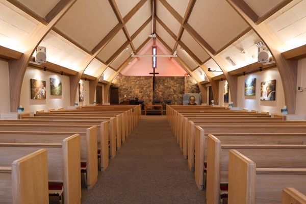 Interior of a church with wooden pews, cross, and artwork.