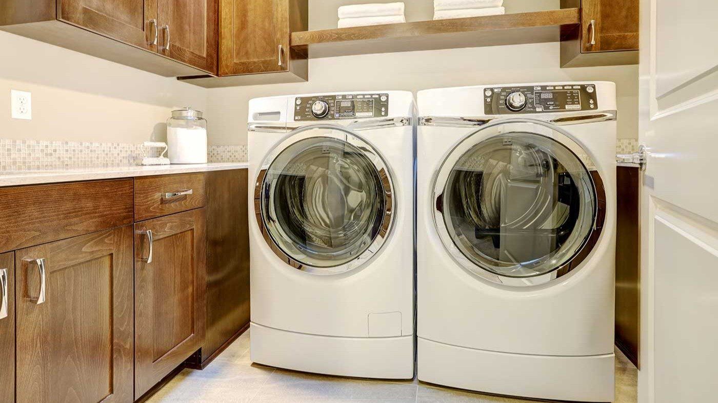 White and brown laundry room features modern appliances placed under shelves and cabinets.