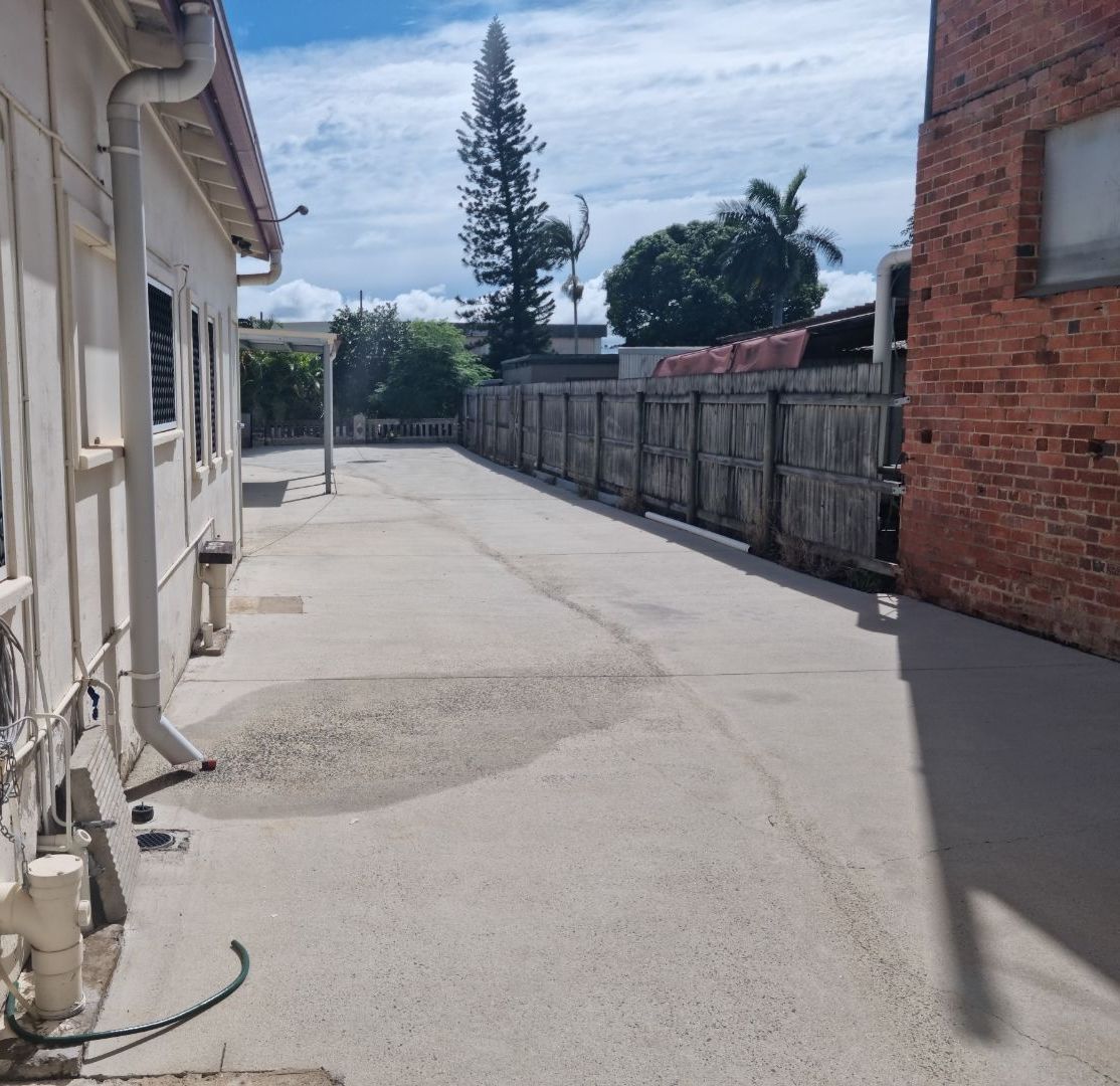 A Woman is Using a Pressure Washer to Clean a Driveway — Blast H2O In Cannonvale, QLD