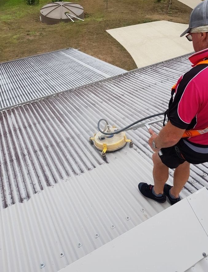 A Man in a Red Shirt is Cleaning the Roof of a House — Blast H2O In Cannonvale, QLD