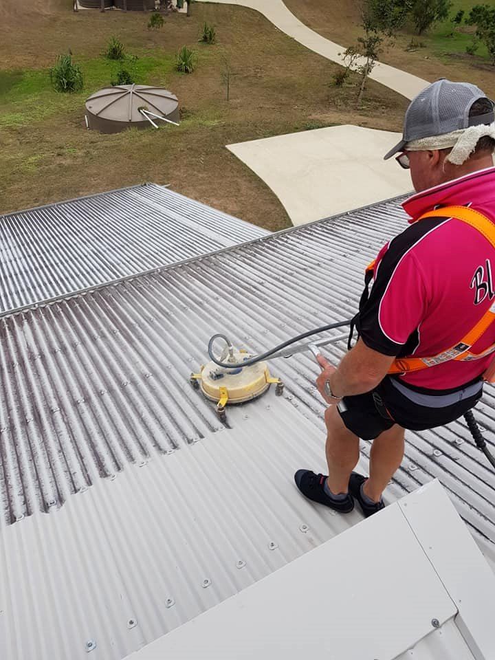 A Man is Cleaning the Roof of a Building With a Machine — Blast H2O In Proserpine, QLD