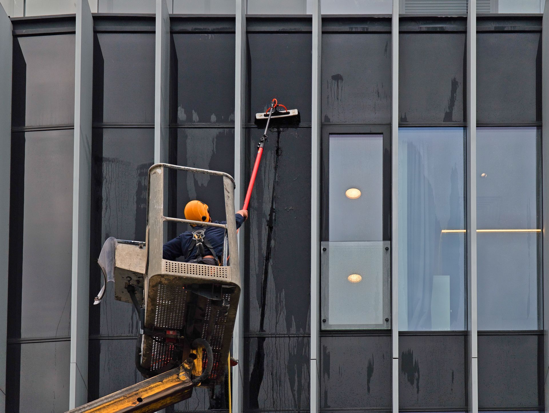 Worker in a suspended lift cleaning a glass building facade.