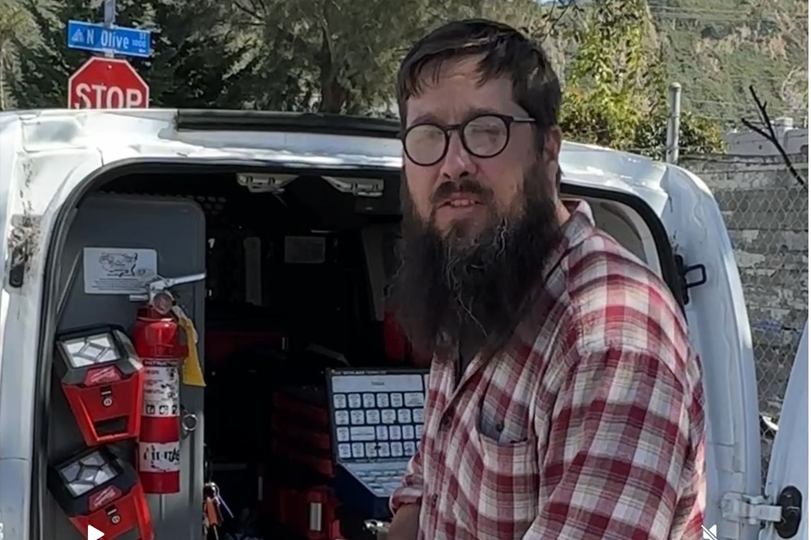 A man with a beard and glasses is standing in front of a white van.
