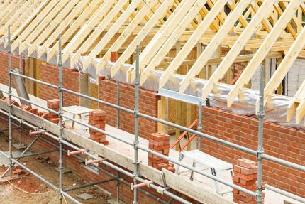 A Brick Wall is Being Built on a Construction Site With Scaffolding — East Coast Roof Tiling Services in Kuluin, QLD