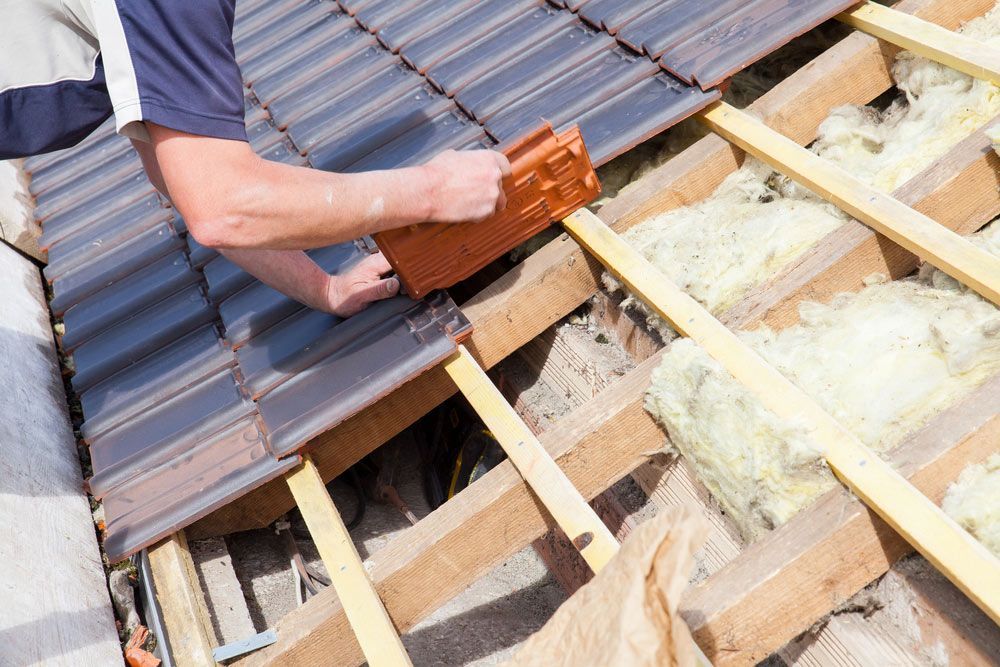 A Man is Installing a Tile Roof on a House — East Coast Roof Tiling Services in Kuluin, QLD