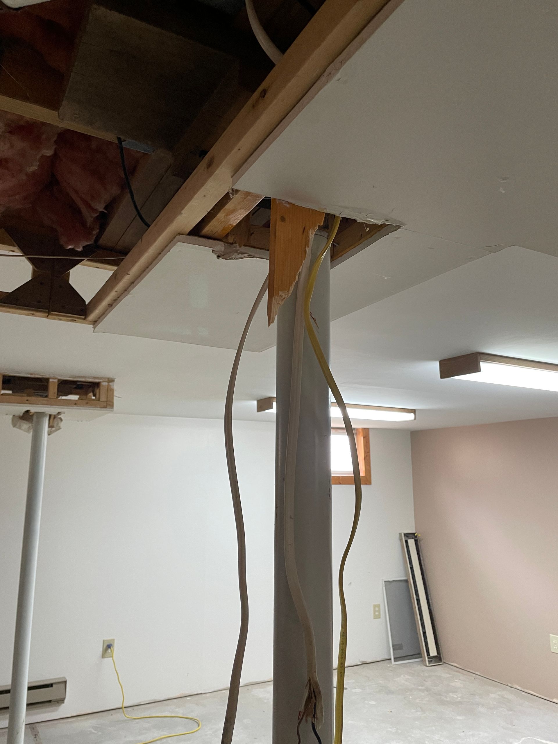 Basement interior with exposed ceiling, support column, wiring, and drywall.