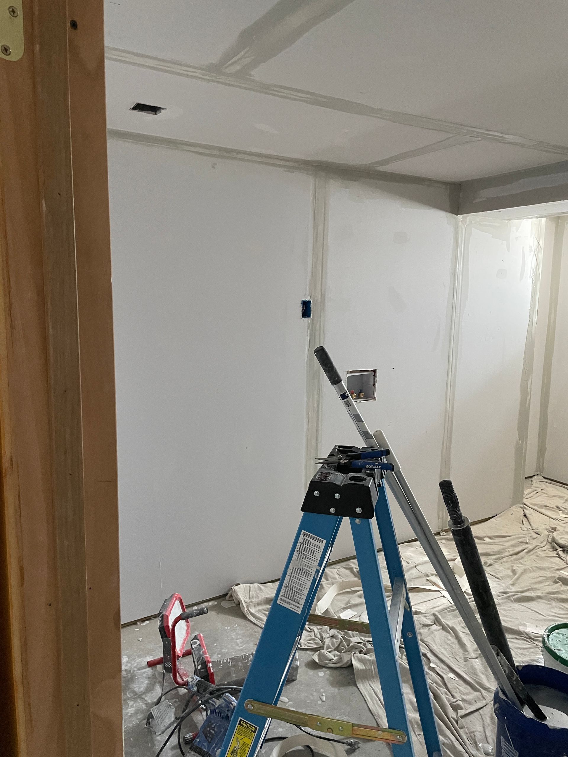 Interior room under construction, blue ladder with painting supplies, drywall.