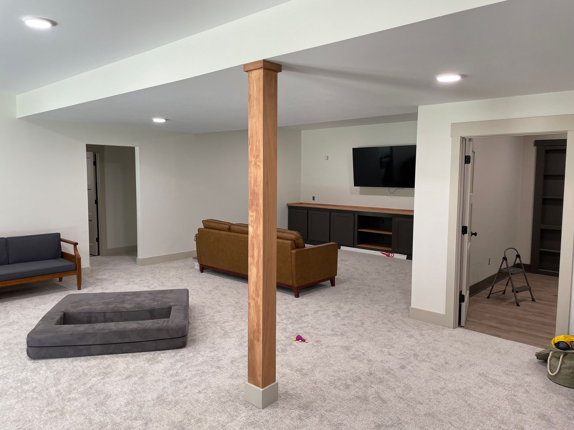 Spacious finished basement with white walls, carpet, and a wooden support beam. Furniture includes couches and a fire pit.