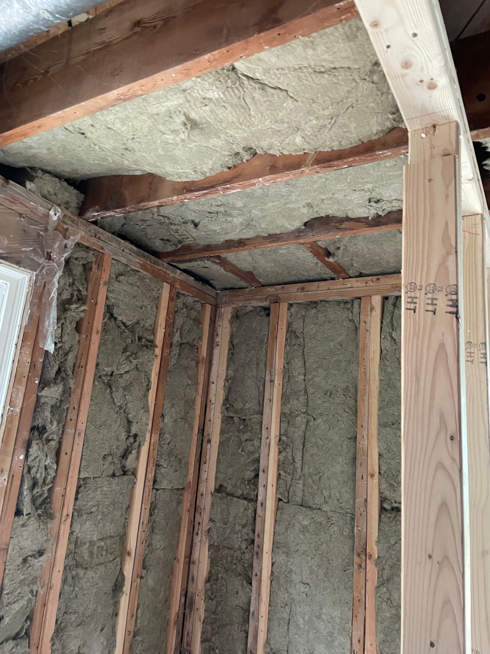 Interior view of a room under construction. Insulation installed in the walls and ceiling. Wooden framing visible.