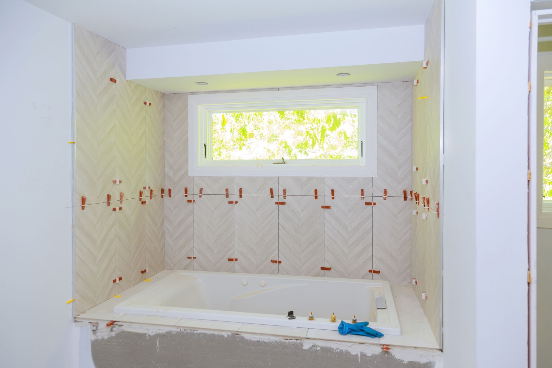 Bathroom with herringbone tile backsplash and window above the bathtub; construction in progress.