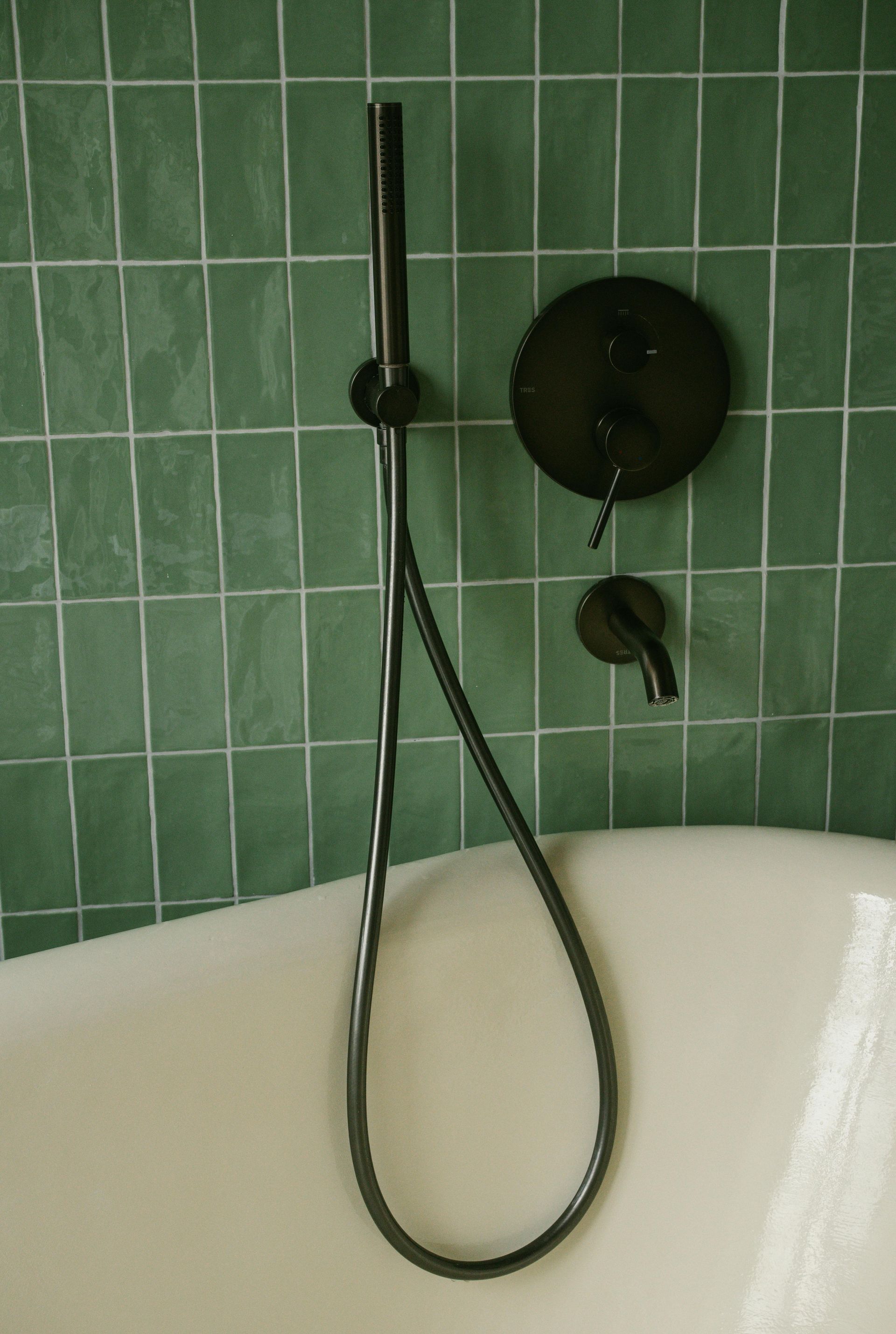 Modern bathroom with green tile walls, white tub, and black shower fixtures