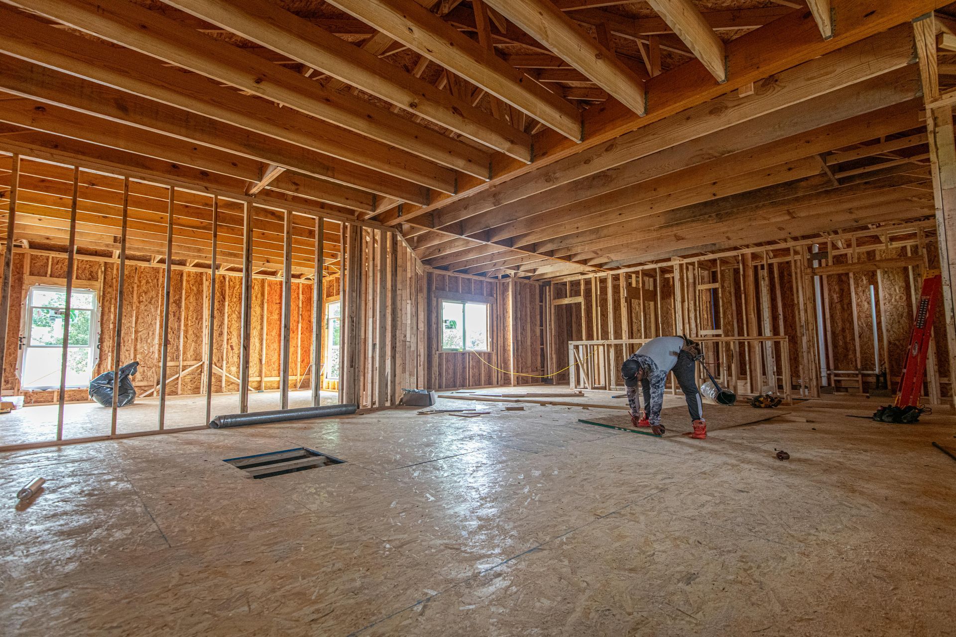 A construction worker installing flooring in the frame of a house addition under construction.