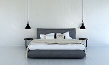Bedroom with a gray bed, white bedding, black pendant lights, and wood side tables against a white wall.