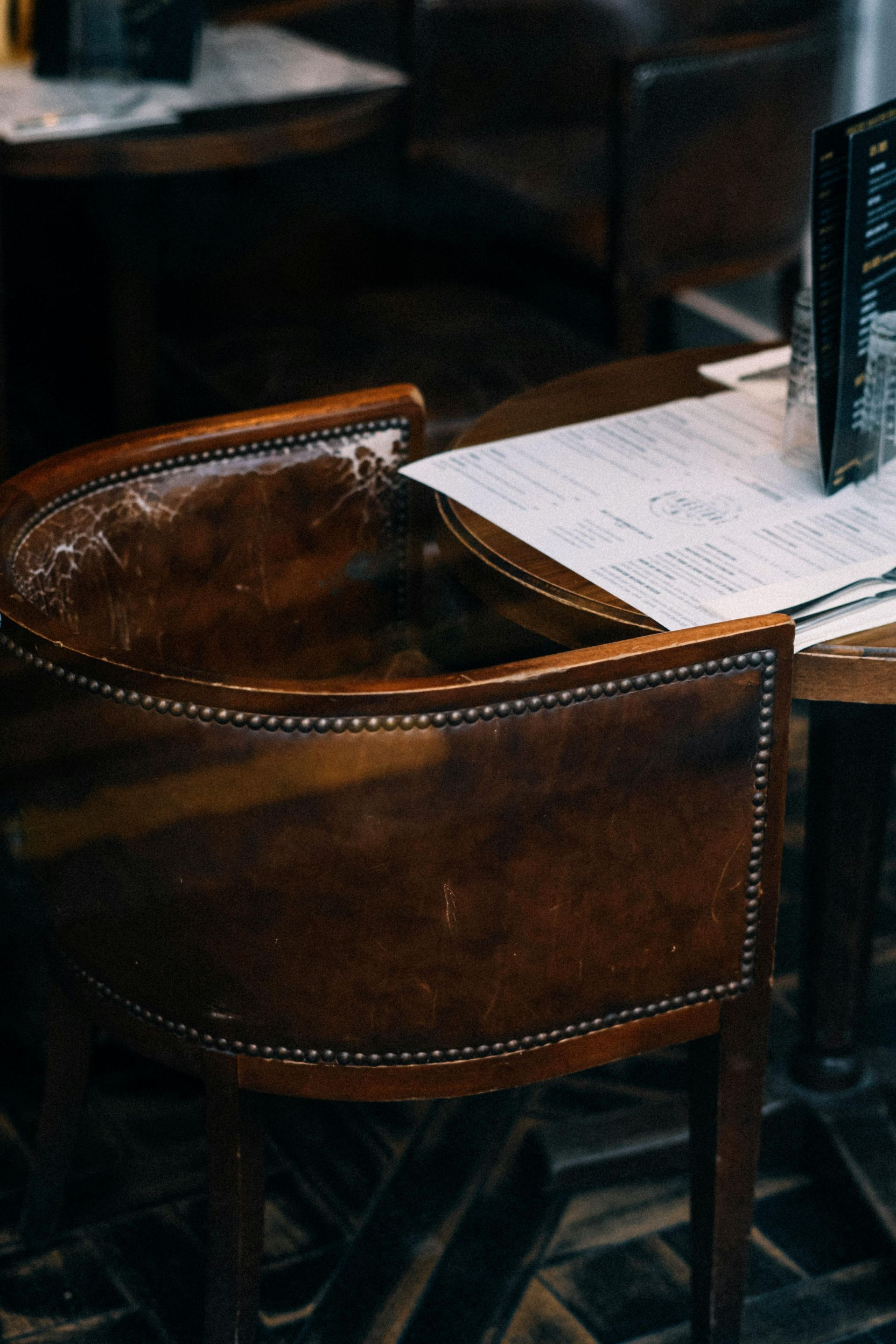 A brown, leather-upholstered armchair with metal stud trim sits at a cafe table with a menu on top.